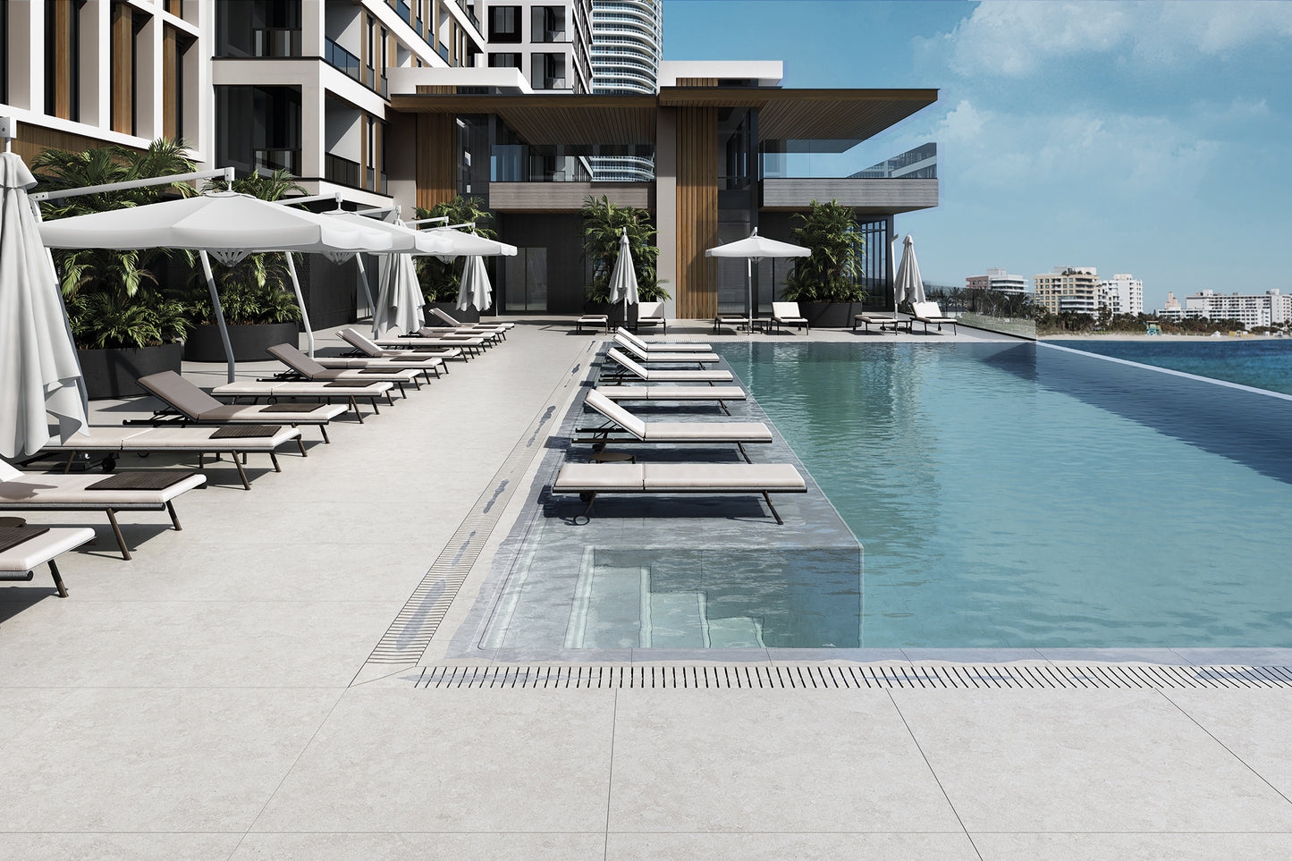 Modern outdoor infinity poolside area with light gray tiled deck, closed white umbrellas, and multiple lounge chairs under a clear blue sky.